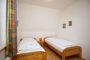 Ein kleines, sauberes Zimmer mit zwei Holzbettchen, einem Nachttisch mit Lampe und einem farbenfrohen Vorhang.