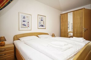 A neatly made bed with white linens, a wooden headboard, and a wooden wardrobe with a mirror. - Apartment near the harbor with balcony and sea view - Hafenhäuser Breege FeWo 11 - (Breege)