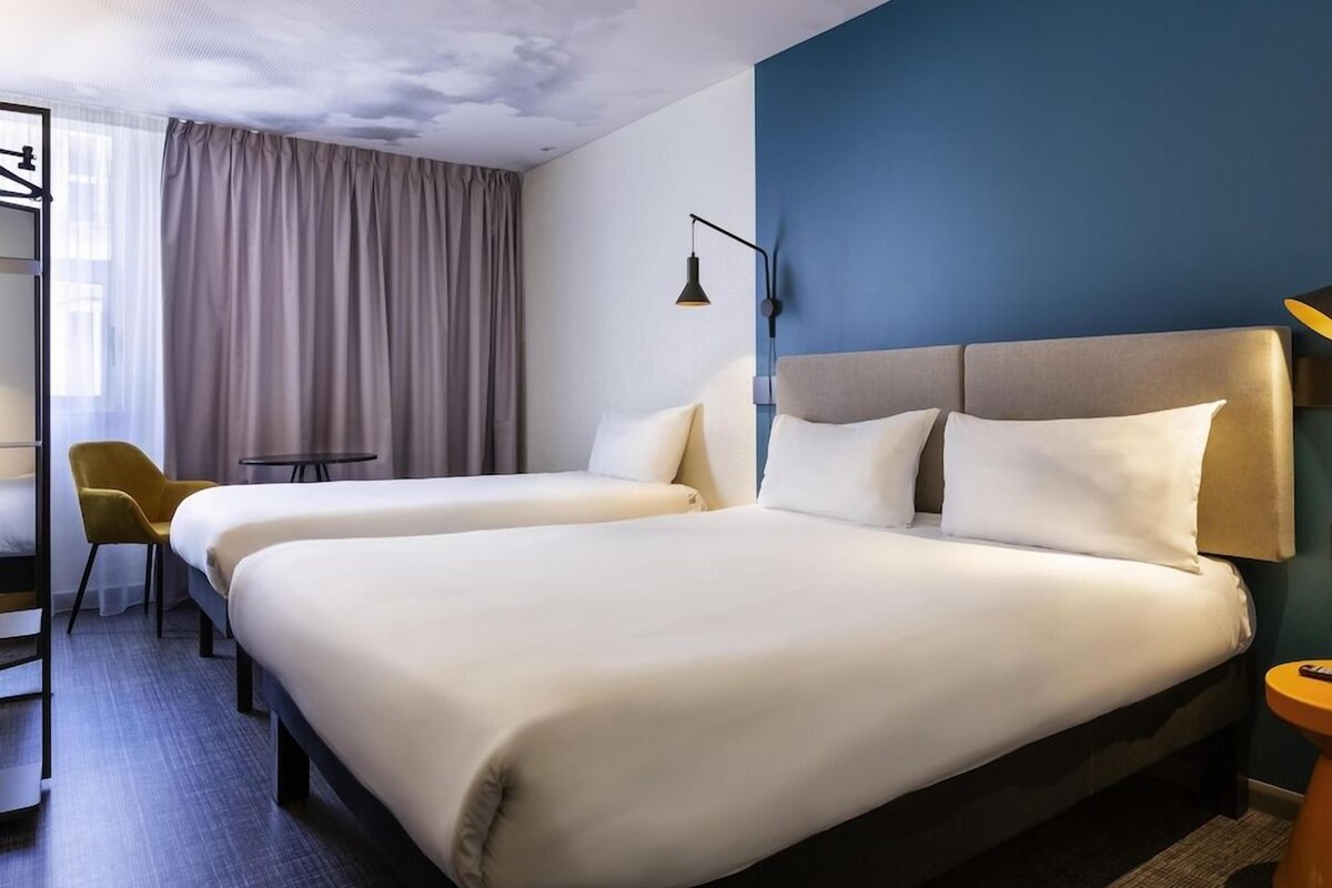 Une chambre d’hôtel avec deux lits, un bureau, une chaise et une lampe.