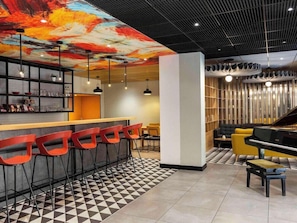 Un espace bar moderne avec des tabourets de bar rouges, un piano et un sol orné d’un motif géométrique.