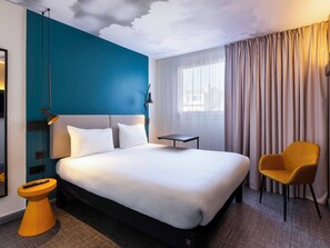 Una camera d'hotel moderna con un letto grande, un tavolino, una sedia e vista sulla città dalla finestra.