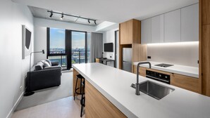 A modern kitchen with a large island, built-in appliances, and a city view. - Nesuto Docklands Apartment Hotel (Docklands)