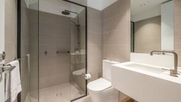 Een moderne badkamer met een douchecabine van glas, een wit wastafelmeubel en een toilet.