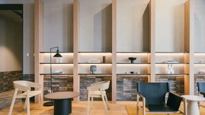 A modern lounge area with wooden chairs, a round table, and a black chair. Shelves with decorative items and a stone wall are in the background. - Nesuto Docklands Apartment Hotel (Docklands)