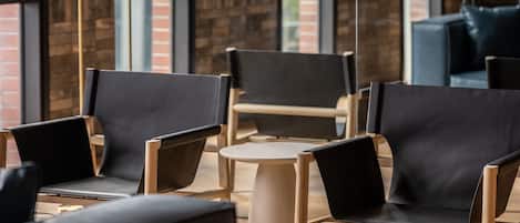A modern lounge area with leather chairs and a round table, brick walls, and large windows.