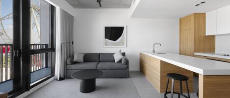 A modern kitchen with a white countertop and wooden cabinets, a gray sofa with a black coffee table, and a large window with a view of a Ferris wheel.