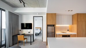 A modern hotel room with a large bed, a desk, and a kitchenette. - Nesuto Docklands Apartment Hotel (Docklands)