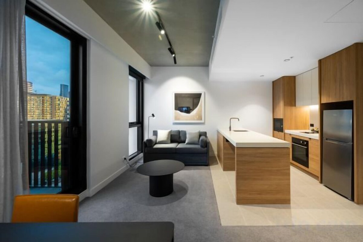 Una cocina moderna con una isla central, un comedor con sofá y vistas de la ciudad a través de amplios ventanales.
