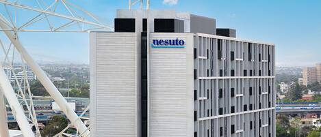 A modern building with a prominent 'nesuto' sign, a Ferris wheel in the background, and a view of the cityscape.