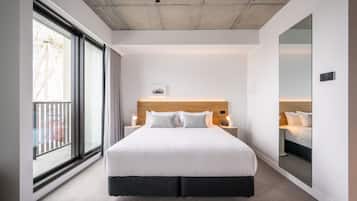 A modern hotel room with a large bed, a wooden headboard, a large window with a view, and a mirror on the wall.