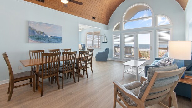 A spacious living area with a dining table and chairs, a blue sofa, and a large window with a view.