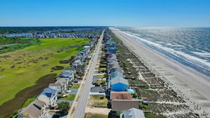 A coastal residential area with houses along a beachfront, a clear sky, and a road running through the middle.