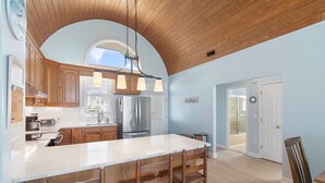 A kitchen with wooden cabinets, a large island with bar stools, stainless steel appliances, and a wooden ceiling.