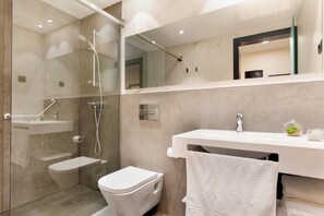 Uma casa de banho moderna com chuveiro em cabine de vidro, sanita e lavatório com uma toalha pendurada na parede.