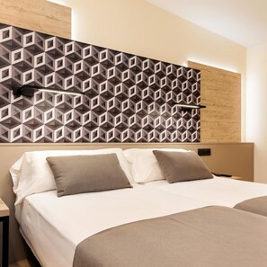 Quarto de hotel moderno com cabeceira estampada em padrão geométrico, cama com lençóis brancos e duas almofadas, e mesa de cabeceira de madeira.