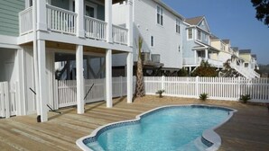 Un barrio residencial con piscina, terraza de madera y casas con balcones y vallas blancas.