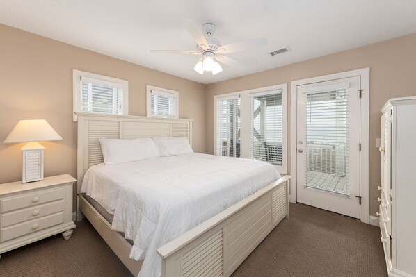 A bedroom with a bed, nightstand, lamp, ceiling fan, and two windows with blinds.