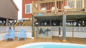A pool area with a wooden deck, two blue chairs, and a 'Beach Life' sign. - Hobbs Realty - Enjoy sunny "Beach Daze" in your private pool and hot tub in this oceanfront home. (Holden Beach)