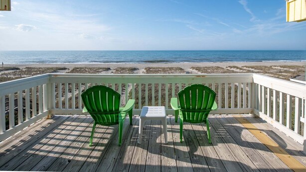 Terraza de madera con dos sillas verdes y una pequeña mesa, con vista a la playa.