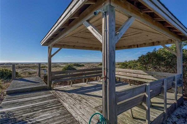 A wooden deck with a covered seating area, overlooking a beach.