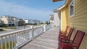 A wooden deck with white railings, red chairs, and a view of residential buildings. - Hobbs Realty - “Casa Del Mar” | 4BR Marsh-View Home w/ Private Gazebo (Holden Beach)