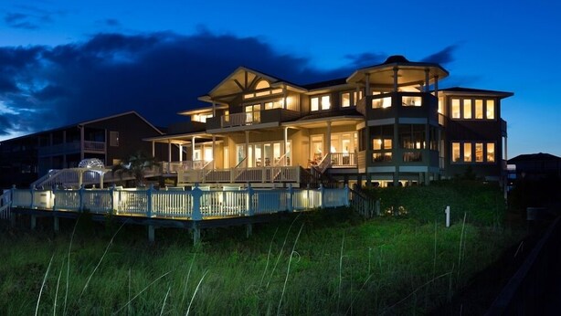 A large, multi-story house with a prominent balcony and a covered porch area. - Hobbs Realty - Oceanfront with Heated Pool, Elevator, and Hot Tub (Holden Beach)