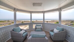 A covered outdoor seating area with wicker furniture and a view of the beach. - Hobbs Realty - Oceanfront with Heated Pool, Elevator, and Hot Tub (Holden Beach)