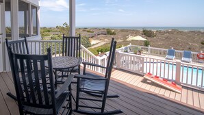 A wooden deck with a table and chairs, a pool, and a view of the ocean. - Hobbs Realty - Oceanfront with Heated Pool, Elevator, and Hot Tub (Holden Beach)