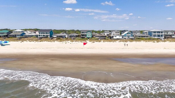 Une propriété située en bord de mer, avec une plage de sable, des vagues et une rangée de maisons marquées par un drapeau.
