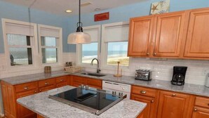 Una cocina con armarios de madera, encimera de granito, estufa integrada y vistas a la playa desde las ventanas.