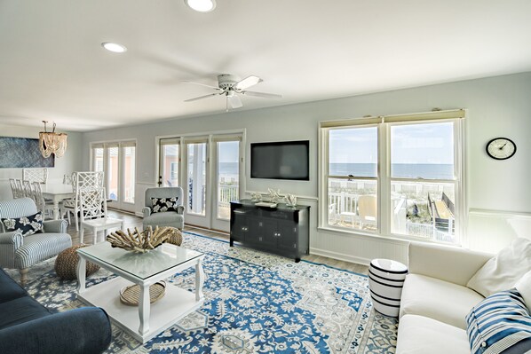 Enjoy the ocean view from the large window in this living room, featuring a flat-screen TV, comfortable seating, and a ceiling fan.