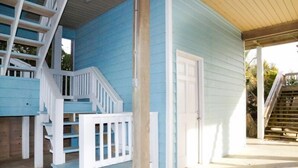 A two-story house with a blue exterior, white front porch, and a wooden staircase. - Hobbs Realty - Enjoy the views in “Clover Reach,” a cute four-bedroom oceanfront home! (Holden Beach)