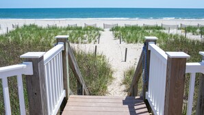 A wooden boardwalk leading to a beach with a wooden fence and grassy dunes.