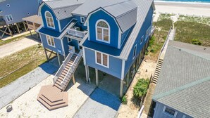 A two-story house with a balcony, a staircase, and a view of the beach.