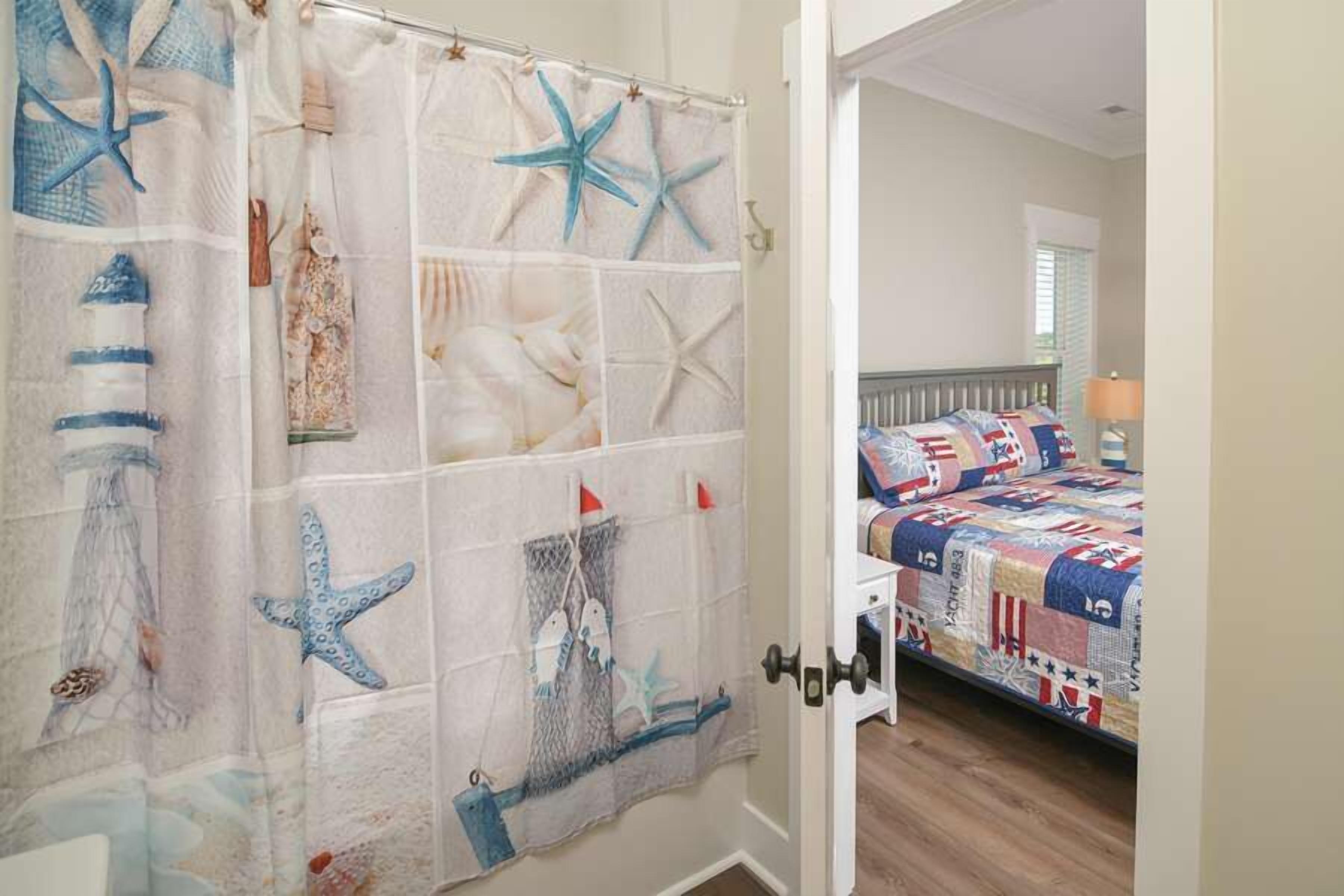 A bedroom with a bed covered in a patchwork quilt, a door with a starfish and seashell curtain, and a view into the room.
