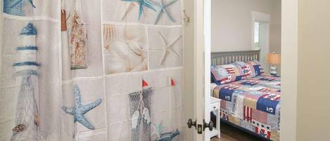 A bedroom with a bed covered in a patchwork quilt, a door with a starfish and seashell curtain, and a view into the room.