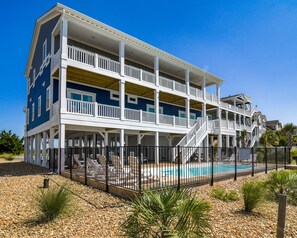 Un edificio de varios pisos con balcones, piscina y ubicación frente a la playa.
