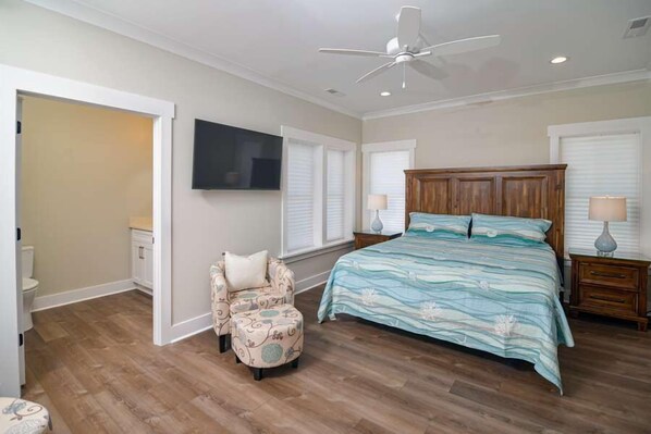 A bedroom with a large bed, a ceiling fan, and a TV mounted on the wall.