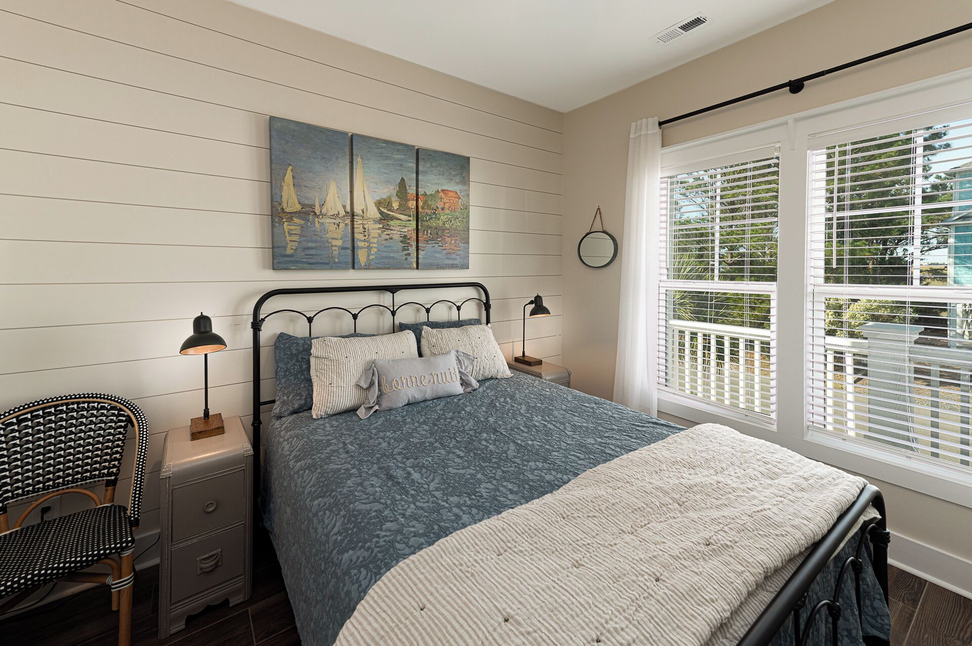 A bedroom with a bed, bedside tables, a chair, a painting, and a window with blinds.