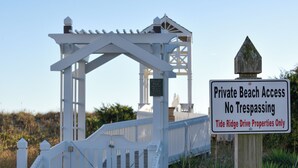 A wooden boardwalk leading to a white gazebo with a sign indicating private beach access and no trespassing for Tide Ridge Drive properties. - Hobbs Realty - “Holden 5” | Elegant Stay w/ Elevator, Private Heatable Pool & Panoramic Views (Holden Beach)
