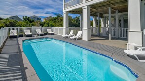 A swimming pool with lounge chairs and a covered deck area. - Hobbs Realty - “Holden 5” | Elegant Stay w/ Elevator, Private Heatable Pool & Panoramic Views (Holden Beach)