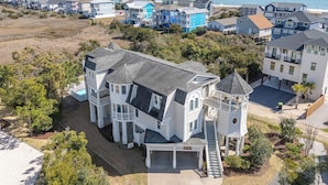 A large, multi-story house with a prominent tower, surrounded by a coastal neighborhood. - Hobbs Realty - “Holden 5” | Elegant Stay w/ Elevator, Private Heatable Pool & Panoramic Views (Holden Beach)