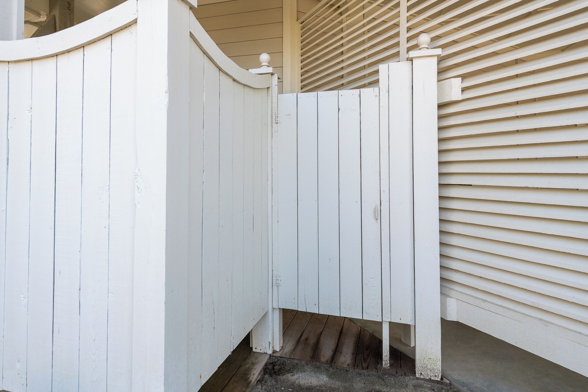 A white wooden gate, a concrete step, and a beige exterior wall with horizontal siding.