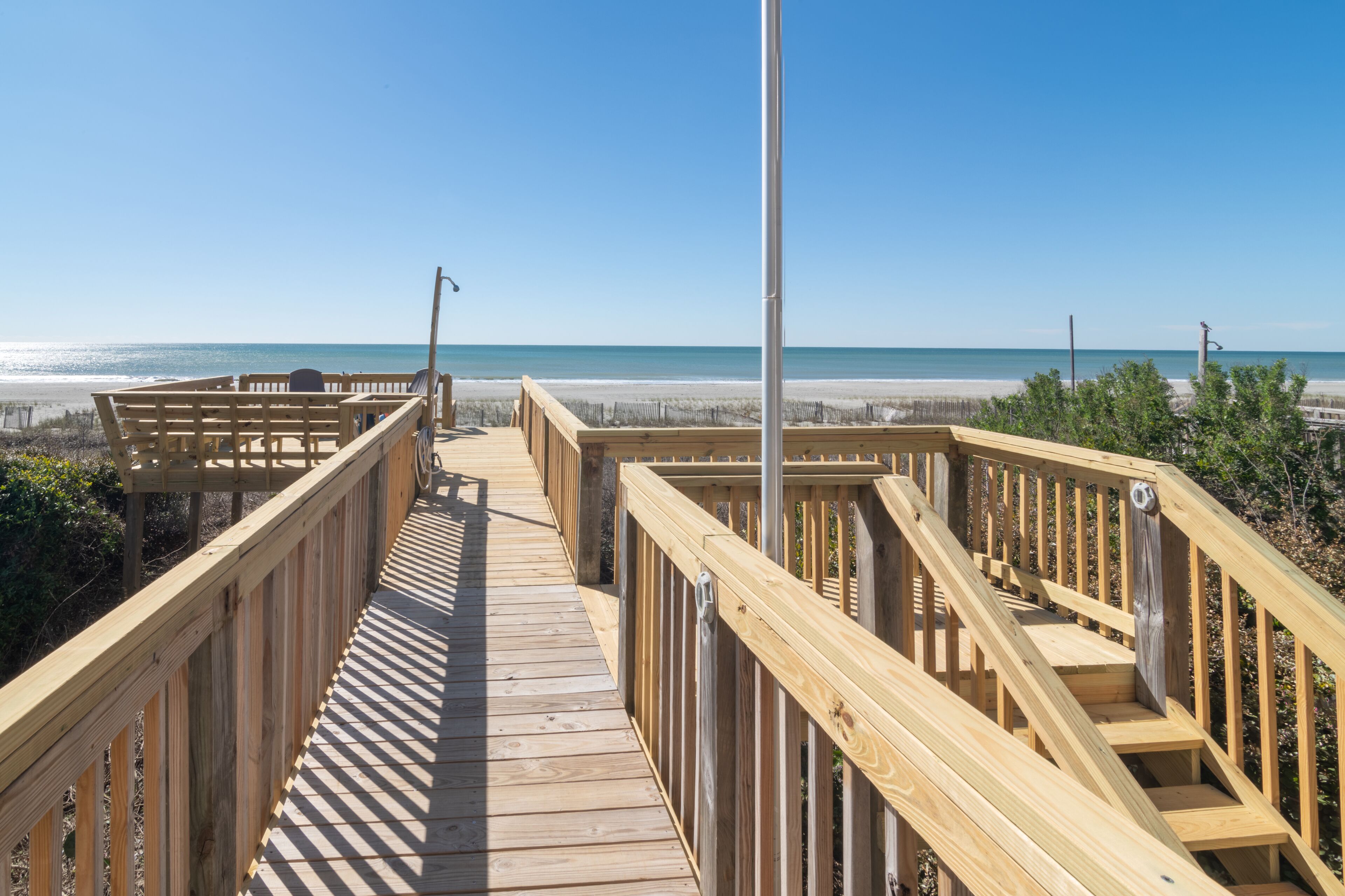 A wooden boardwalk leading to a beach with a clear view of the ocean.