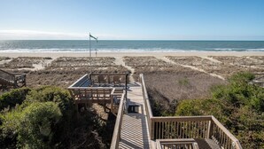 A wooden boardwalk leading to beach access, with a wind indicator and chairs on the side.