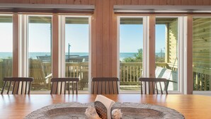 A wooden dining table with chairs, a stone centerpiece, and large windows with a view of the beach.