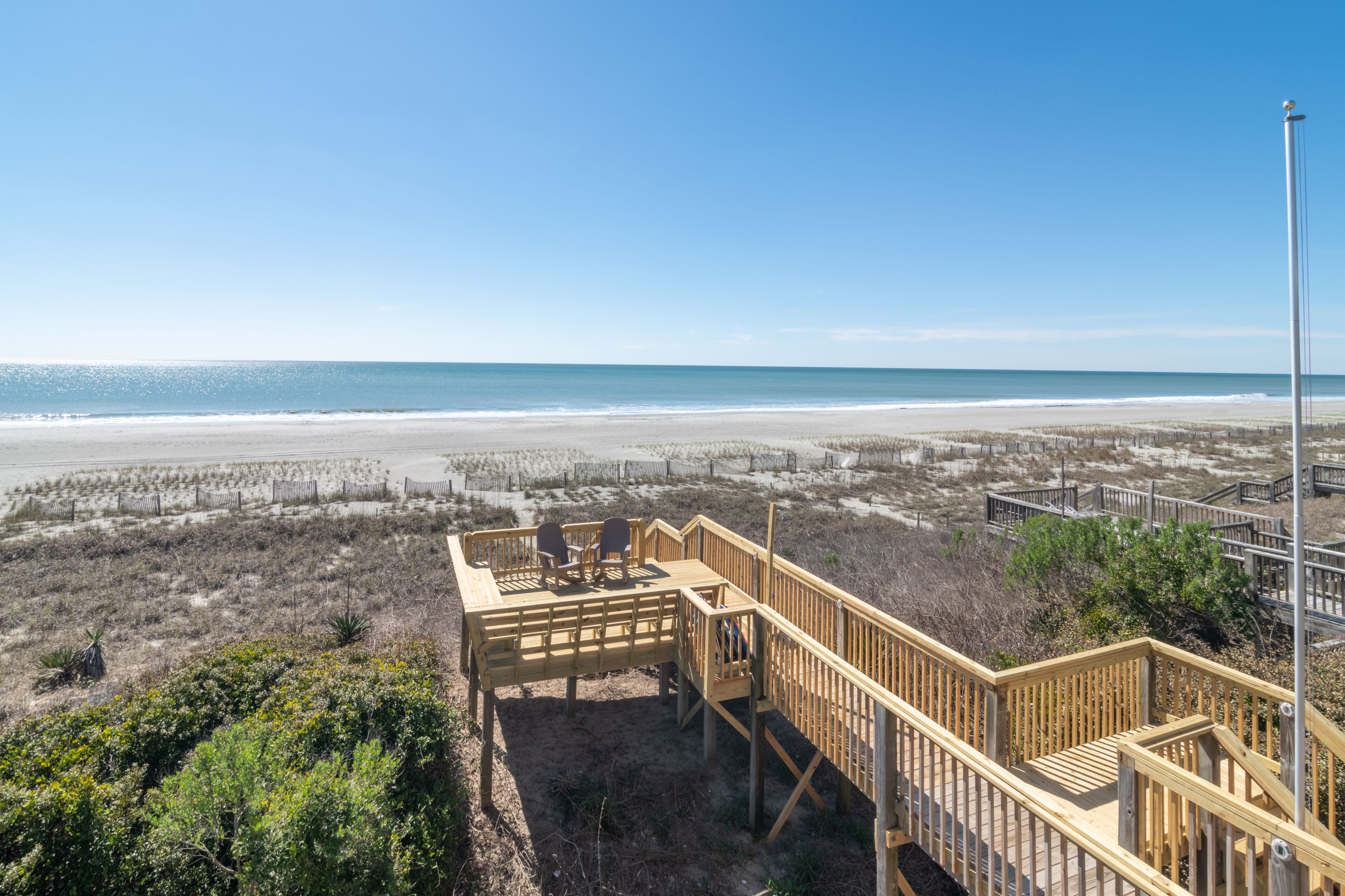 A beach view with a wooden deck and chairs overlooking the ocean.