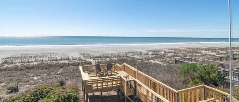 A beach view with a wooden deck and chairs overlooking the ocean.