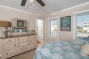 Un dormitorio con cama, cómoda y un espejo grande. Hay una ventana con persianas y un cartel en la pared.