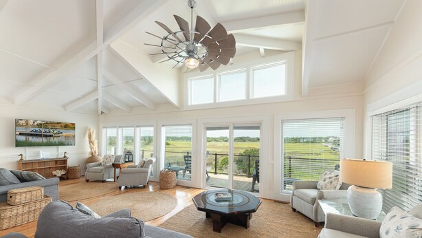 A spacious living room with a high ceiling, large windows, and a ceiling fan.